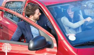 A male is greeted by a female driver as he enters a red car by the passenger side.