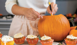 A woman carving a pumpkin and making halloween themed cupcakes.