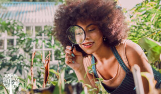 A smiling woman looks through a magnifying glass in a garden.